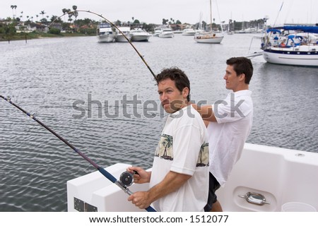 Two men fishing on a yacht hooked up to  large fish