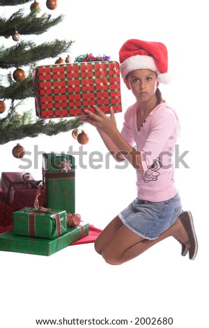 A young girl in a Santa cap shaking a gift under the Christmas tree to see if she can figure out what it might be