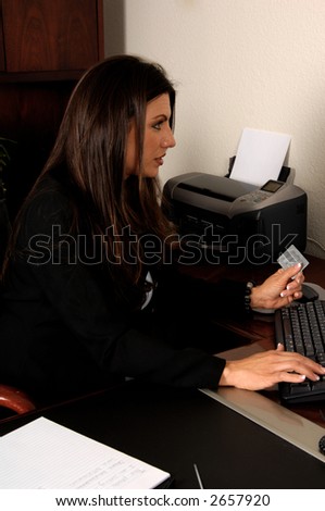 A business woman sitting at her personal computer holding a credit card and making a purchase on line
