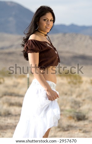 Beautiful Latina woman in a white skirt and brown blouse standing in the desert