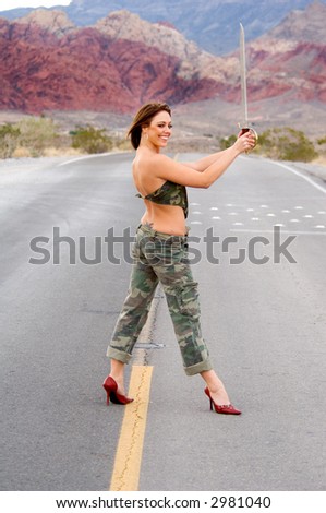 Portrait of a woman with a sword in fatigues and standing at guard in the middle of a road in the desert