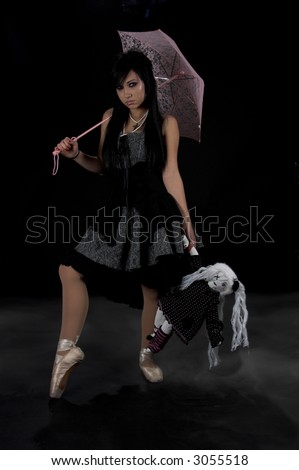 Beautiful raven haired gothic girl dancing in the fog with a pink parasol and a sad little doll
