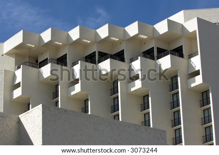 Architectural detail of the top four floors of a resort hotel set against a blue sky. Detail shows cube and stair step z shaped design