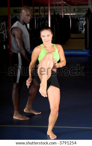 Young female MMA fighter working on high knee kicks with her personal trainer in the gym