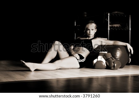 Beautiful MMA fighter sitting on the gym floor with her gloves and reclined against a heavy bag after a long workout