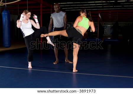 Young female MMA fighters working on body kicks with their personal trainer in the gym
