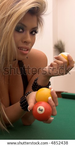 Sexy young Asian bikini model laying on her belly on top of a pool table with balls in her hands