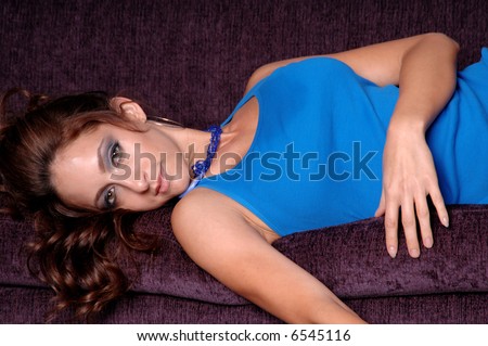 Sexy young model in a blue tank top laying on her side on a purple couch