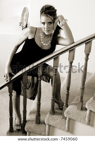 Young woman in a black cocktail dress and crystal necklace and bracelet leaning against a banister