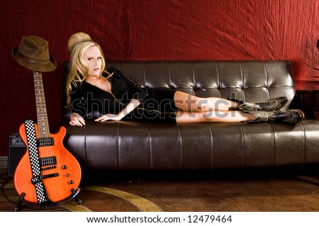 Beautiful young woman laying on a leather couch in a black knit dress and cowboy boots