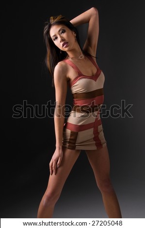 Beautiful young Asian woman with long black hair dressed in a sexy little stripped mini dress on a grey background