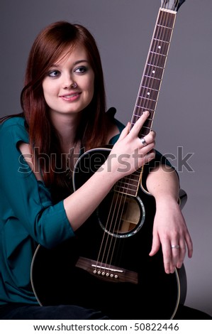 Pretty young redheaded guitar player sitting cross legged with her acoustic guitar