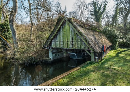 Run down thatched boathouse, in need of repair, on Norfolk Broads surrounded by trees