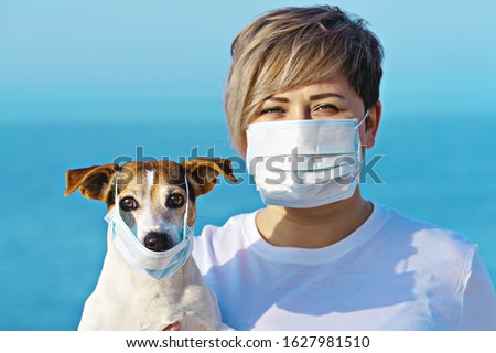 Woman in protective surgical mask holds dog pet in face mask. Chinese Coronavirus disease COVID-19 is dangerous for pets