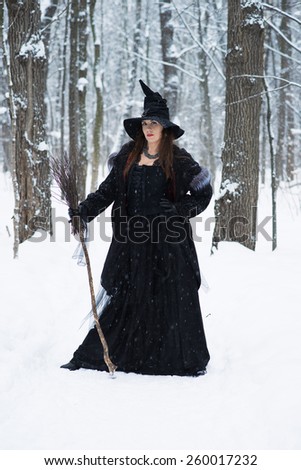 Woman in witch\'s hat holding broom in winter forest