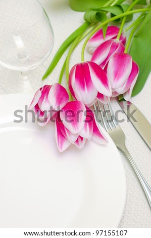 Tender pink tulips grace a table setting . Sample copy space provided with the empty white plate