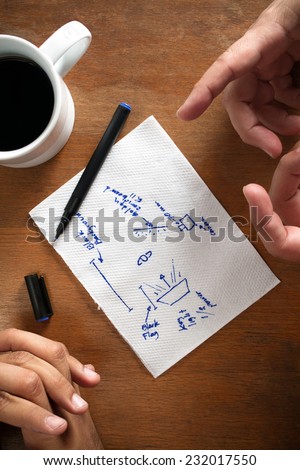 A couple of hands over a wooden table discussing a series of diagrams, drawings can be easily changed or edited in post production software.