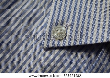 Fragment of shirt close up. Fabric in blue and white stripes with a button.