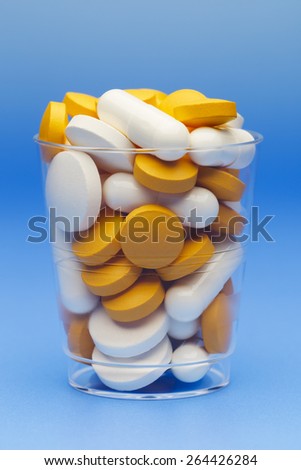 Pills and capsules in a medicine cup.