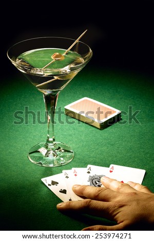 Aces winning card hand laid on green felt poker table with deck of cards and martini pimento olive on cocktail stick