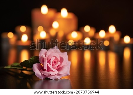 PINK ROSE FOCUSED ON THE GRAVE AND LIGHTED CANDLES UNFOCUSED IN THE BACKGROUND. Foto d'archivio © 