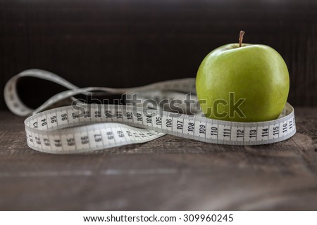 apple surrounded by a measuring tape referring to diet and health concept on wooden background