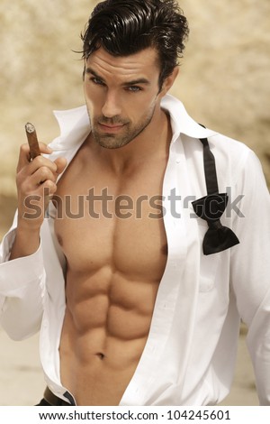 Sexy male model smoking cigar in open formal attire exposing great toned muscular body and abs