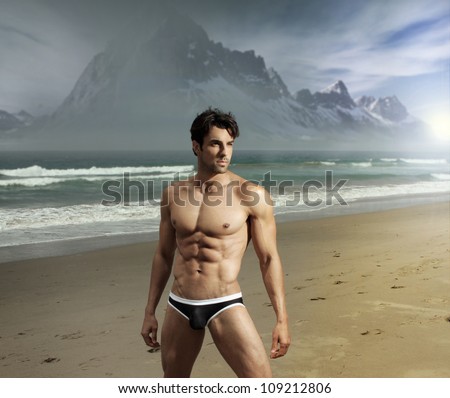Muscular fit sexy guy on remote scenic beach location with dramatic mountains in background