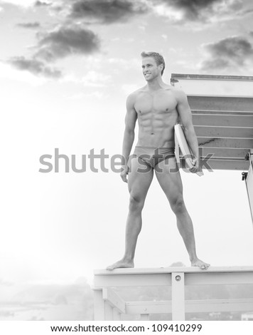 Young fit lifeguard on duty at the beach standing on tower