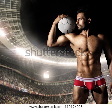 Sexy male model as soccer player in red underwear holding ball in crowded stadium