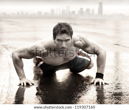 Sexy fit muscular man doing push-up on wet road with city skyline in the background