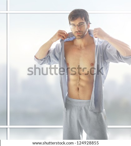 Sexy male model with hot naked body with open shirt against modern background window