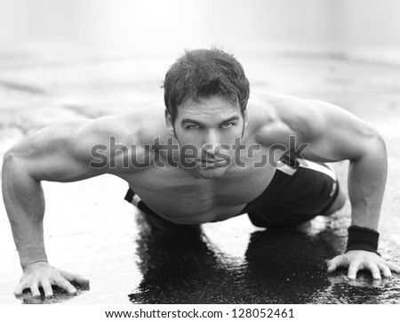 Inspirational portrait of a muscular fit man doing push-ups on wet cement