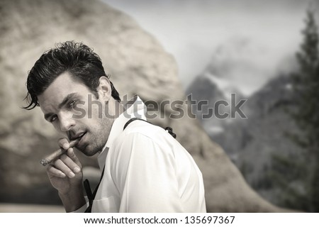 Sexy hunky male model outdoors smoking cigar with seductive look and vintage feel