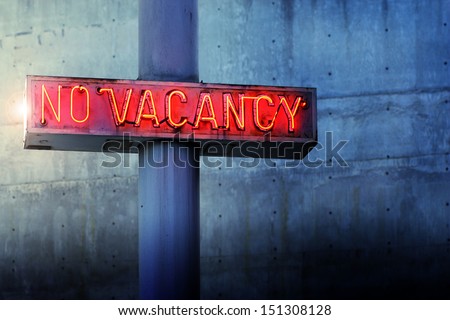 Glowing retro neon \'no vacancy\' sign against cool blue wall background