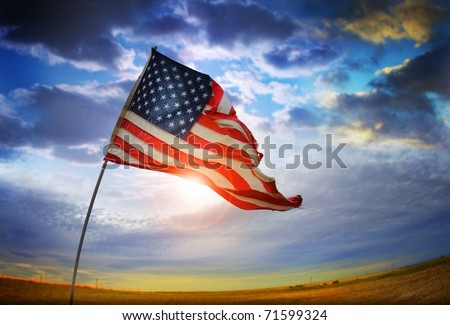 Wide angle photo of a tattered American flag blowing in the wind against a beautiful cloudscape