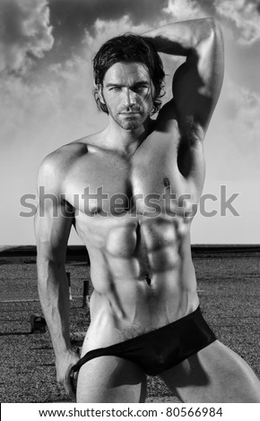 Fine art black and white portrait of a beautiful muscular male model in black briefs in provocative pose outdoors