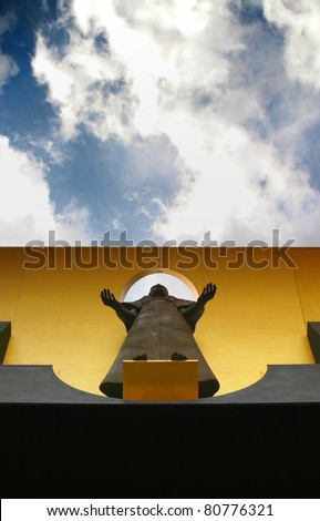 Sculpture of religous figure with hands open taken from below with sky above