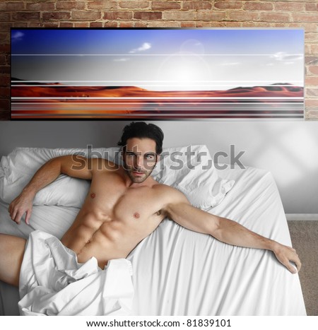 Sexy nude male model laying back in big bed at home in cool loft interior