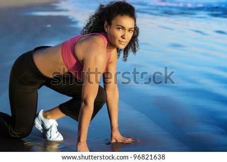 Portrait of an athletic female runner stretching on the beach in twilight near blue water