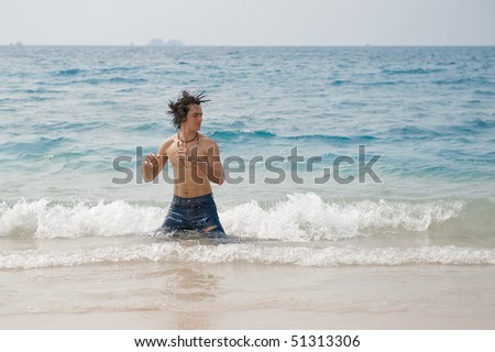 Athletic and muscular man in the surf of the Atlantic Ocean shaking his wet hair.