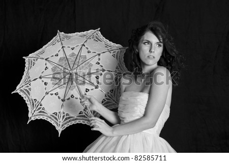 Black and white image of a beautiful woman holding an umbrella on a black background.