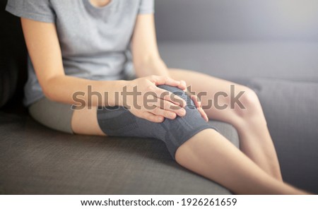 A woman sits on the couch  holds a sick knee with her hands. Problems of orthopedics, disease, trauma Сток-фото © 