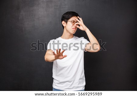 Portrait of disgusted reluctant asian guy shut nose and turn away from nasty awful smell, sniff something rotten, disgusting reek of food, raise hand in stop and refusal gesture, black background Stok fotoğraf © 