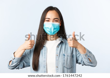 Social distancing lifestyle, covid-19 pandemic everyday life and leisure concept. Supportive enthusiastic asian woman in medical mask thumbs-up, wearing PPE while going grocery shopping