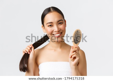 Beauty, hair loss products, shampoo and hair care concept. Close-up of happy attractive asian woman in bath towel showing brush, recommend haircare product for healthy long hair