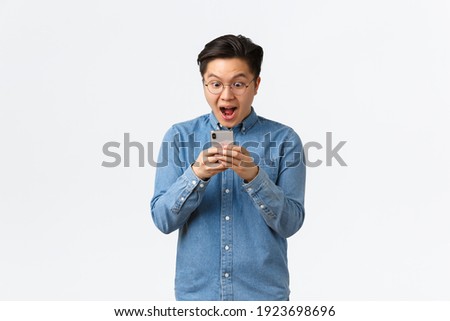 Excited guy seeing new awesome application or social network post of favorite blogger, looking amazed and happy at mobile phone screen, standing amused over white background