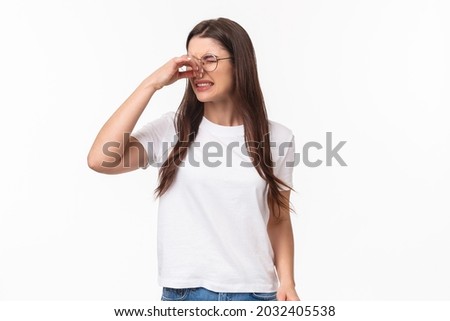 Smells disgusting. Portrait of disgusted and displeased young beautiful girl in glasses, shut nose with fingers and look away with grimace as something have awful smell, reek, stand white background Stok fotoğraf © 