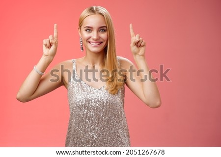 Excited gorgeous blond european woman in silver shiny elegant dress raise hands pointing up showing impressive incredible advertisement smiling happily thrilled wanna take closer look, red background ストックフォト © 