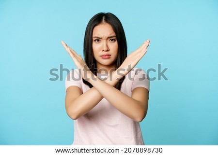 Stop. Concerned asian woman showing cross sign, saying no, raise awareness, standing over blue background 商業照片 © 